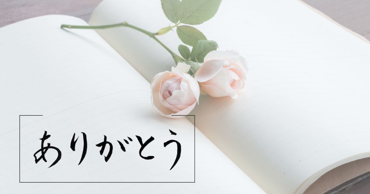 薔薇の花と開いたをノートを背景に、「ありがとう」の筆文字
