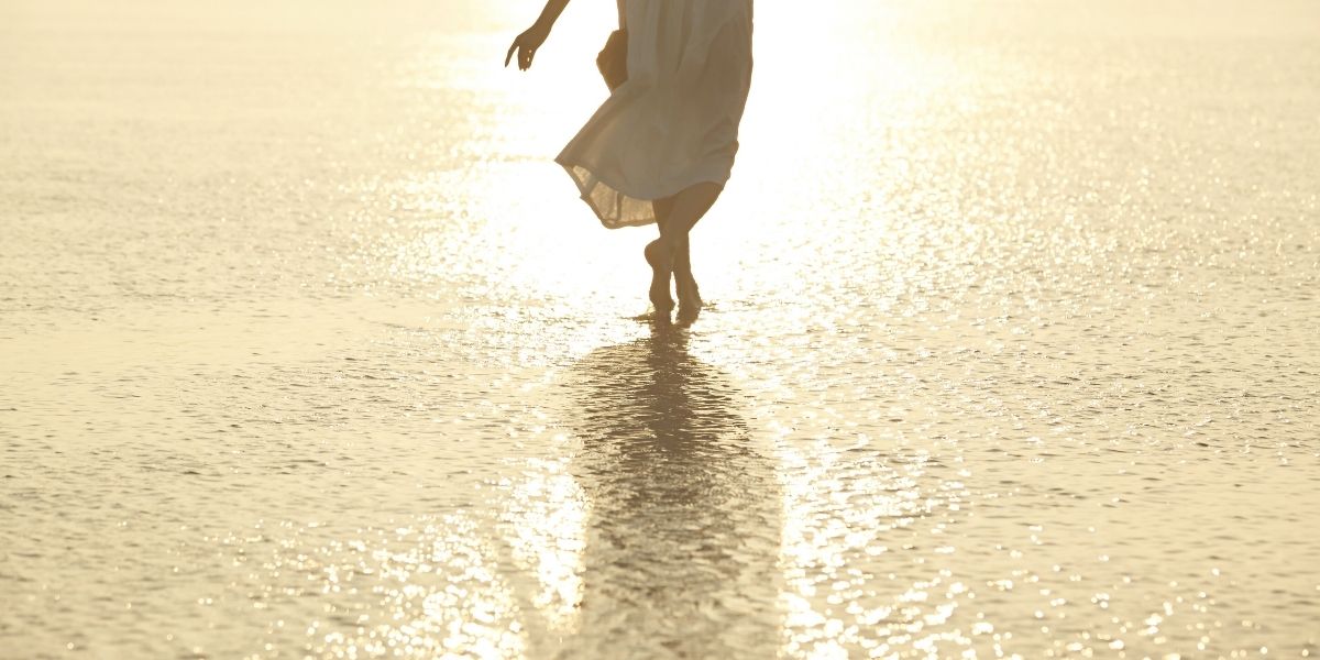夕日がきれいな海辺を歩く女性の後ろ姿。