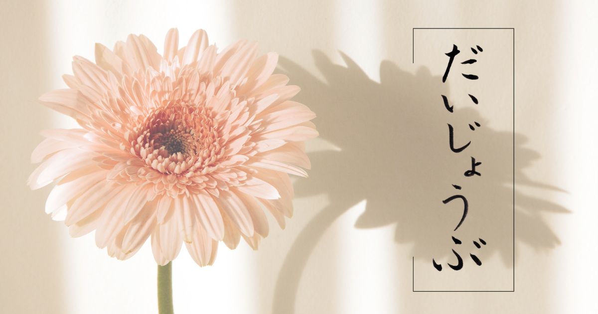筆文字「」だいじょうぶ」。薄ピンクのガーベラとともに。