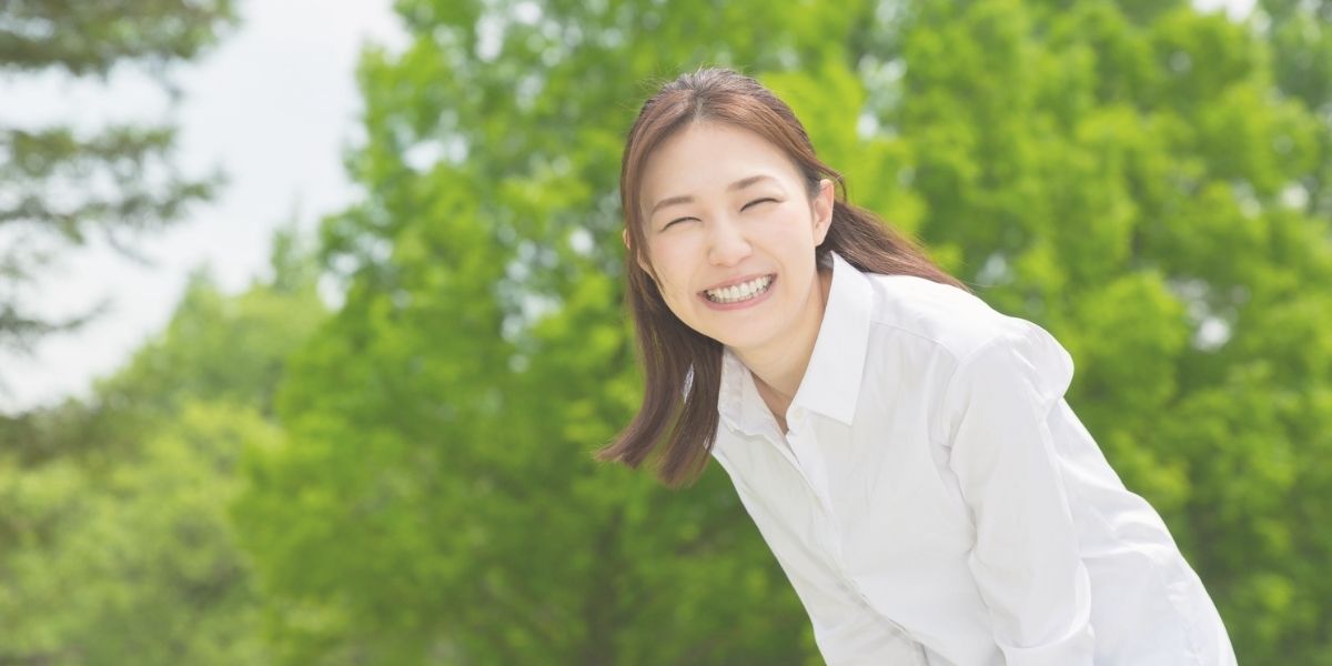 嬉しそうに微笑む女性、背景には、緑の木々が。
