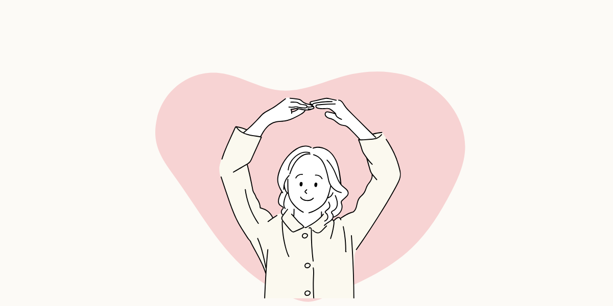 大きなハートマークの前で、両手でOKを作っている女性。