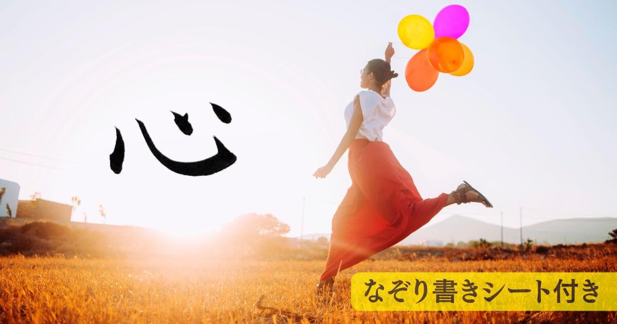 筆文字「心」。背景には草原で子供のように風船を持ってはしゃぐ女性。