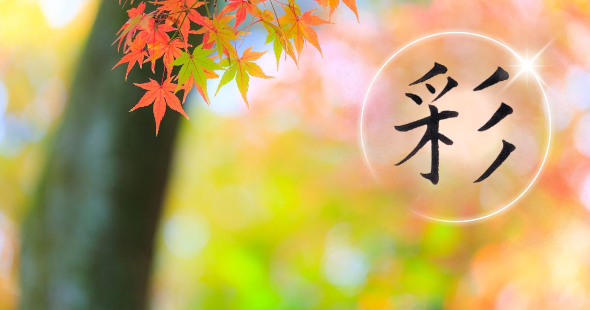 筆文字「彩」。背景には美しい紅葉が青から赤へと紅葉している様子。