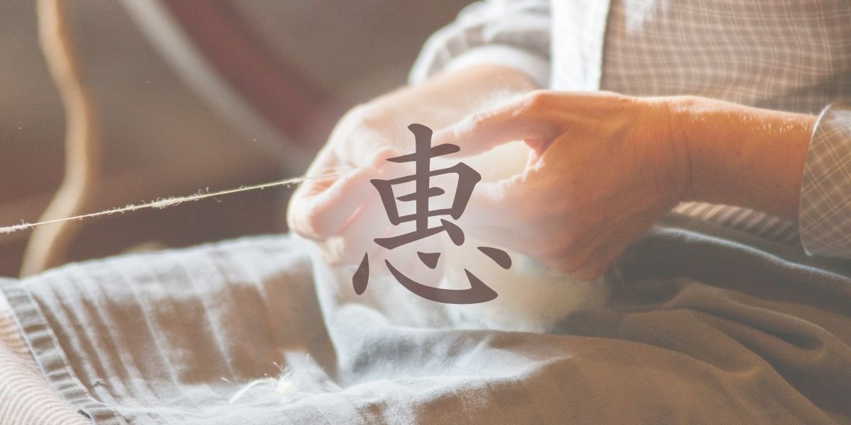 「恵」の旧字「惠」。背景には糸をつむぐ女性の手のアップ。