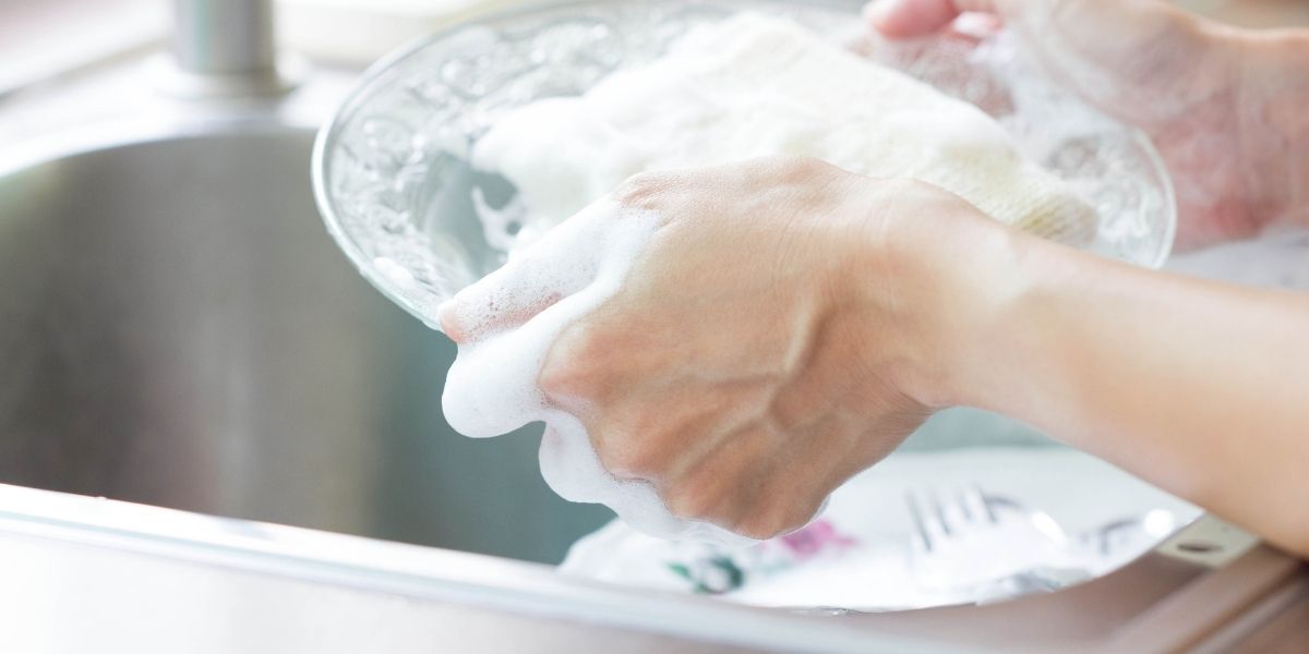 食器を洗っている手のアップ、泡立てたスポンジでガラスの食器を持っている。