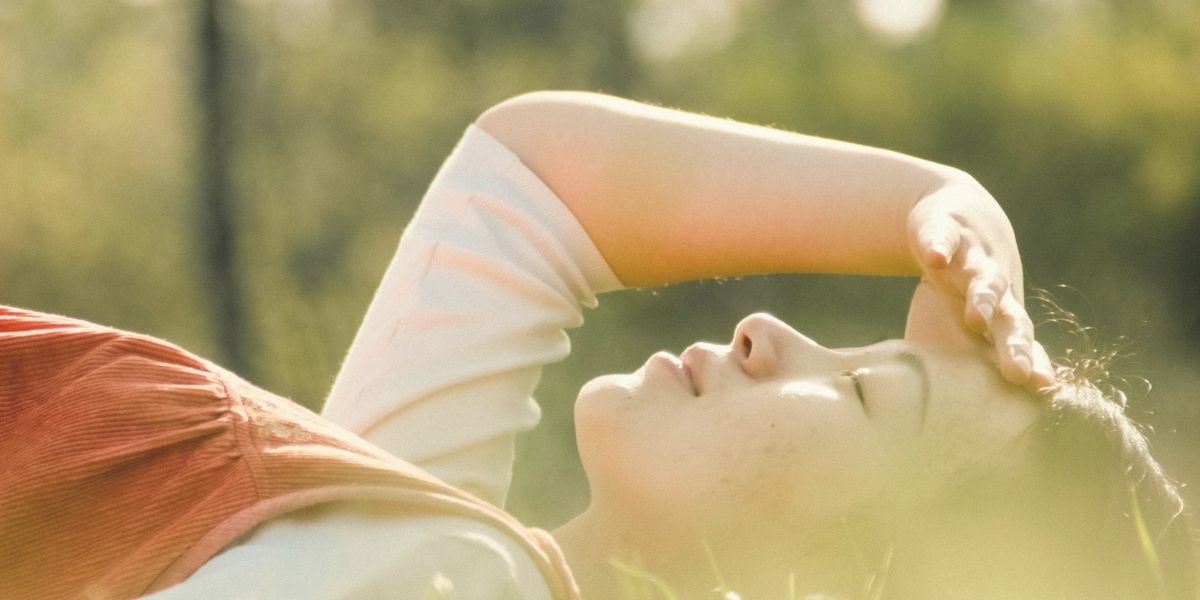 草原の中で気持ちよさそうに寝転んでいる女性。