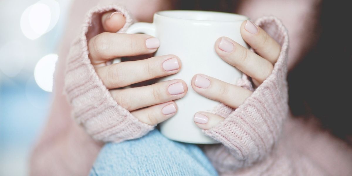 女性の手に大きめの白いマグカップ。両手で持っている。